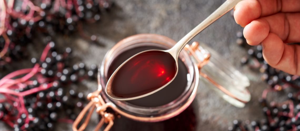 Holundersaft auf Löffel mit Holunder im Hintergrund. Mit Holundersaft die Abwehr im Winter stärken.